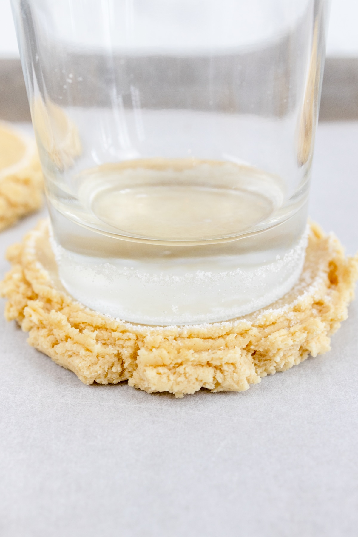 Close up of a glass that has been dipped into sugar flattening cookie dough into a cookie shape. 