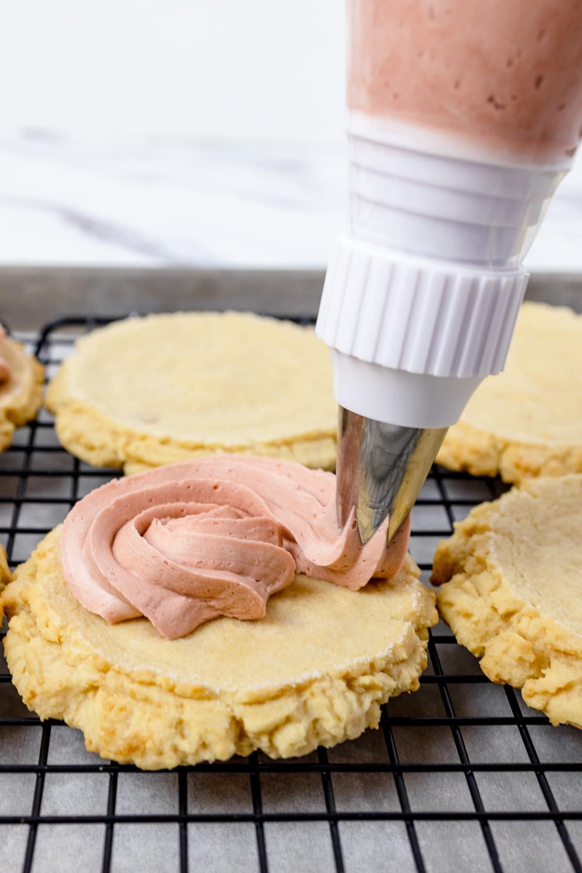 Close up of pink frosting being piped onto a cookie. 