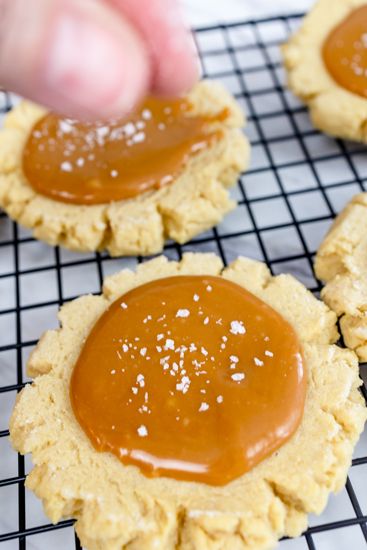 Close up of salted caramel cookies being topped with a pinch of salt. 