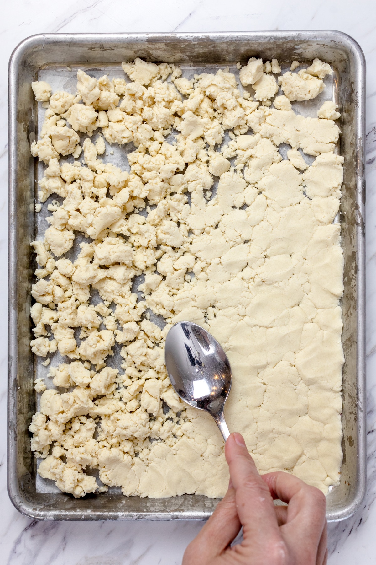 Top view of cookie dough being pressed down into the bottom of a baking sheet.