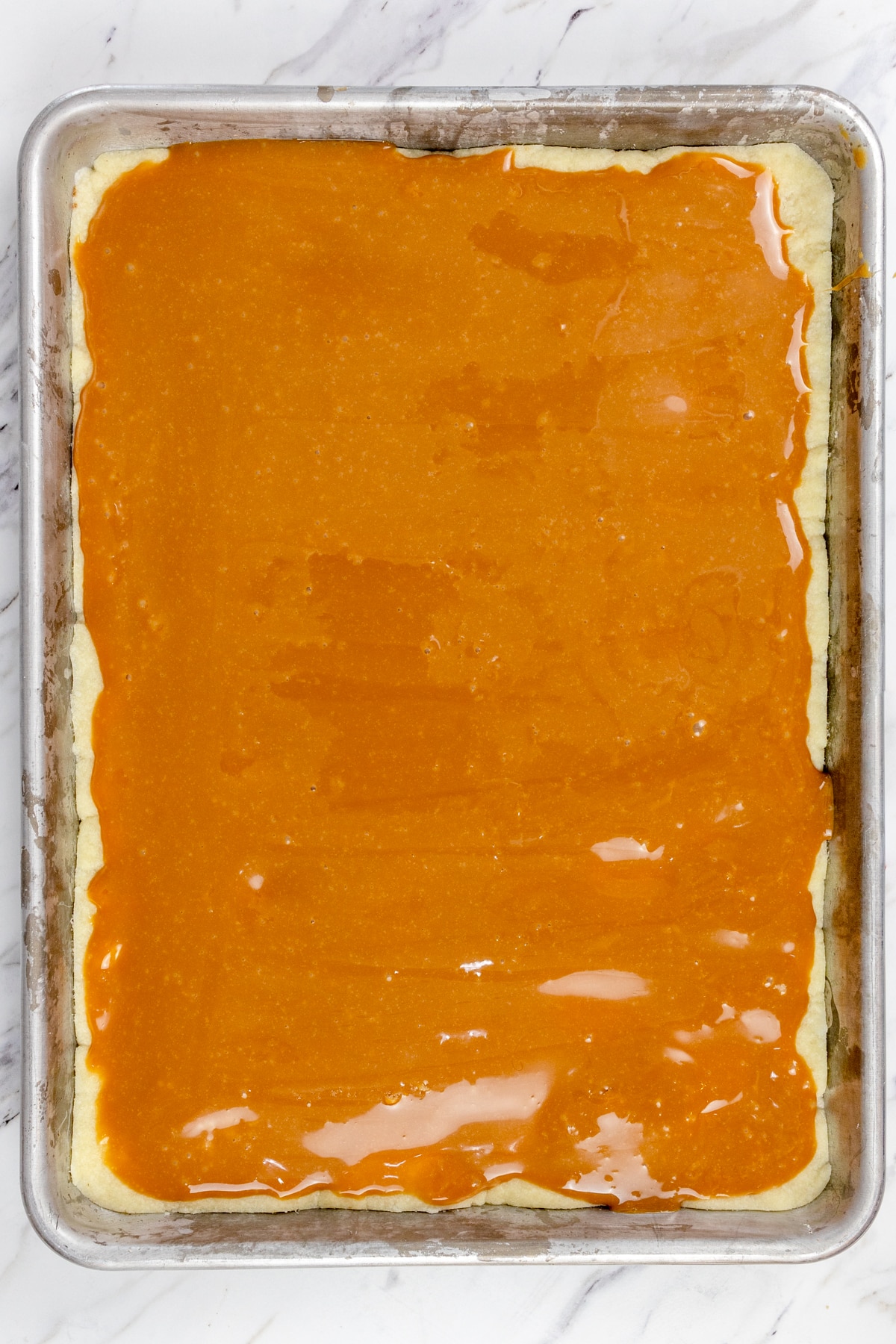 Top view of cookie dough base in a baking tray covered in caramel mix. 