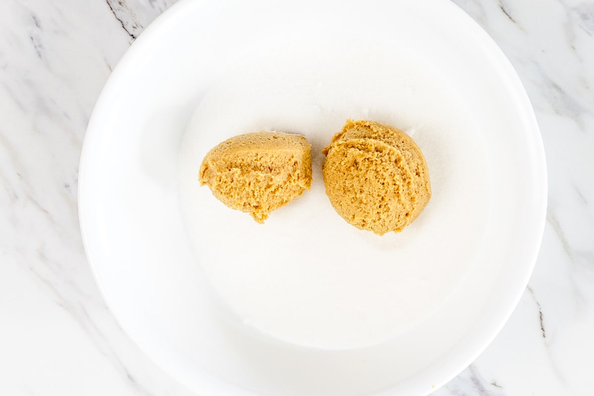Top view of a bowl of sugar with two molasses cookie dough balls in it.