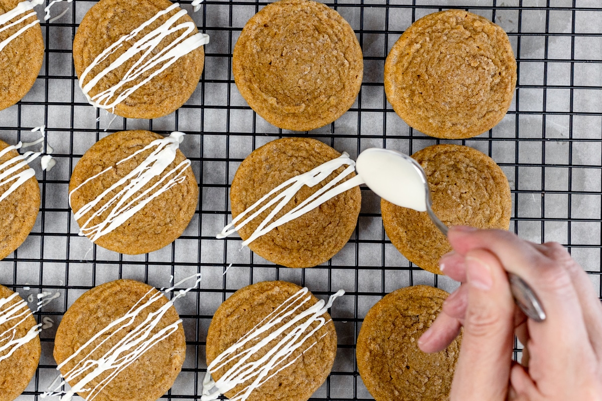 Top view of molasses cookies on a wire rack with melted white chocolate being drizzled on top.