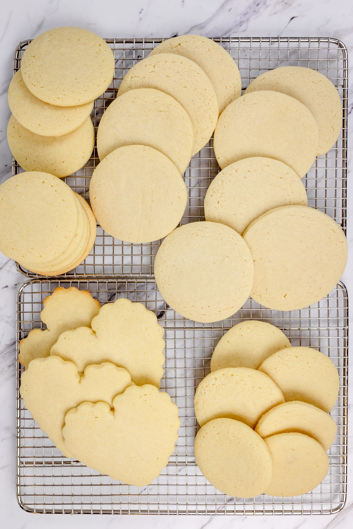 Top view of sugar cookies cut out into hearts and circles on a wire rack.