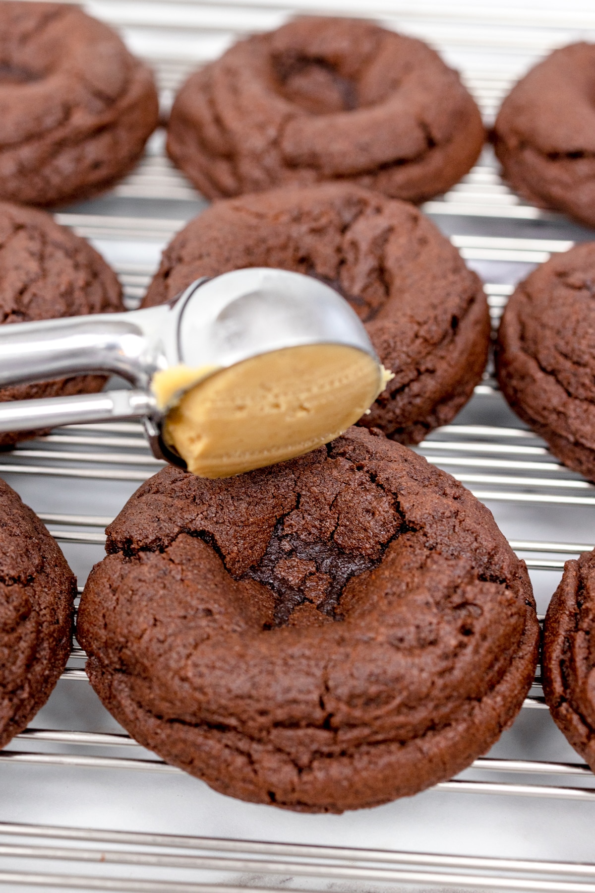 Close up of a chocolate cookie with a well in it, with a small scoop of peanut butter being put into the well of the cookie. 