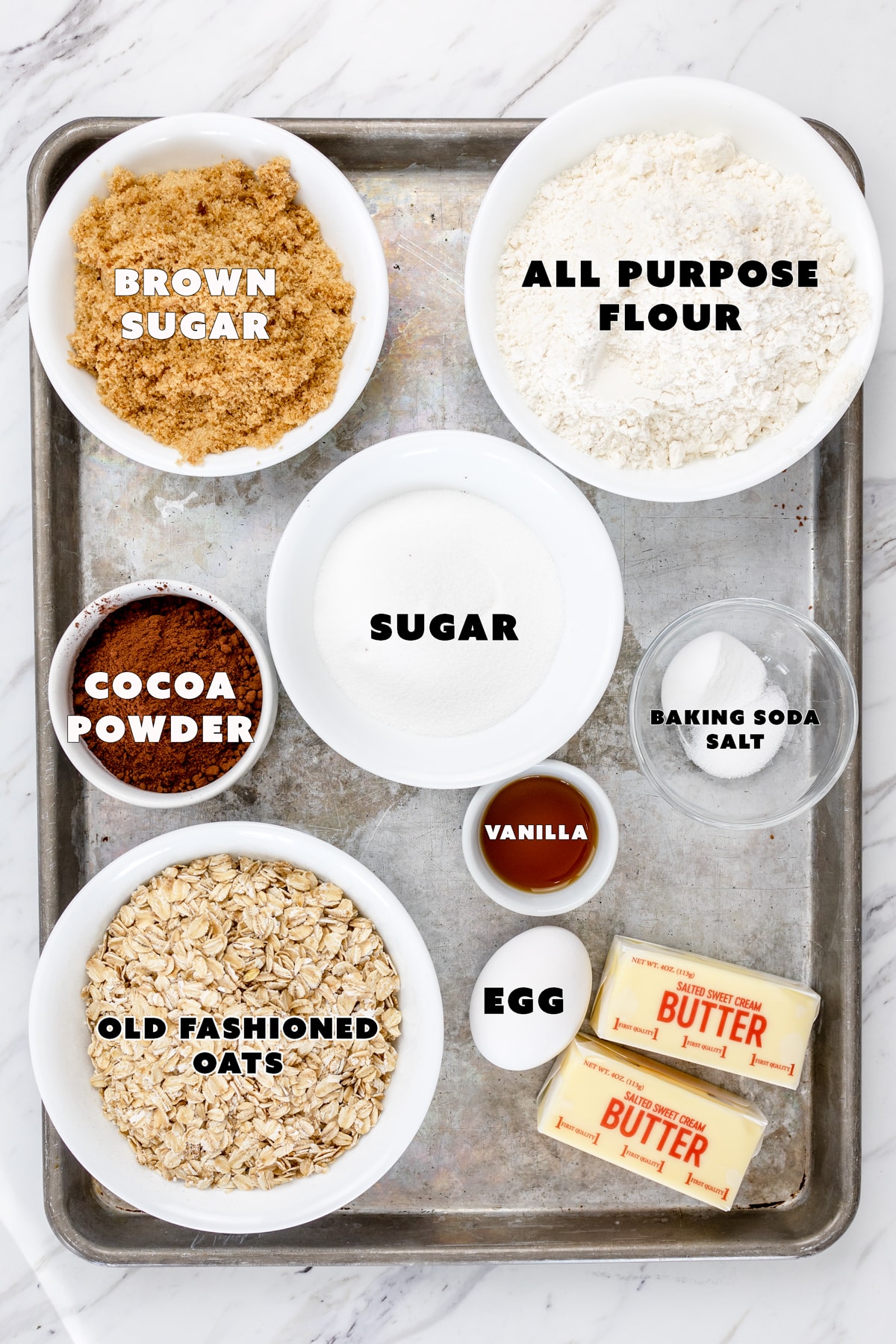 Top view of ingredients needed for chocolate oatmeal cookies in small glass bowls on a baking tray. 