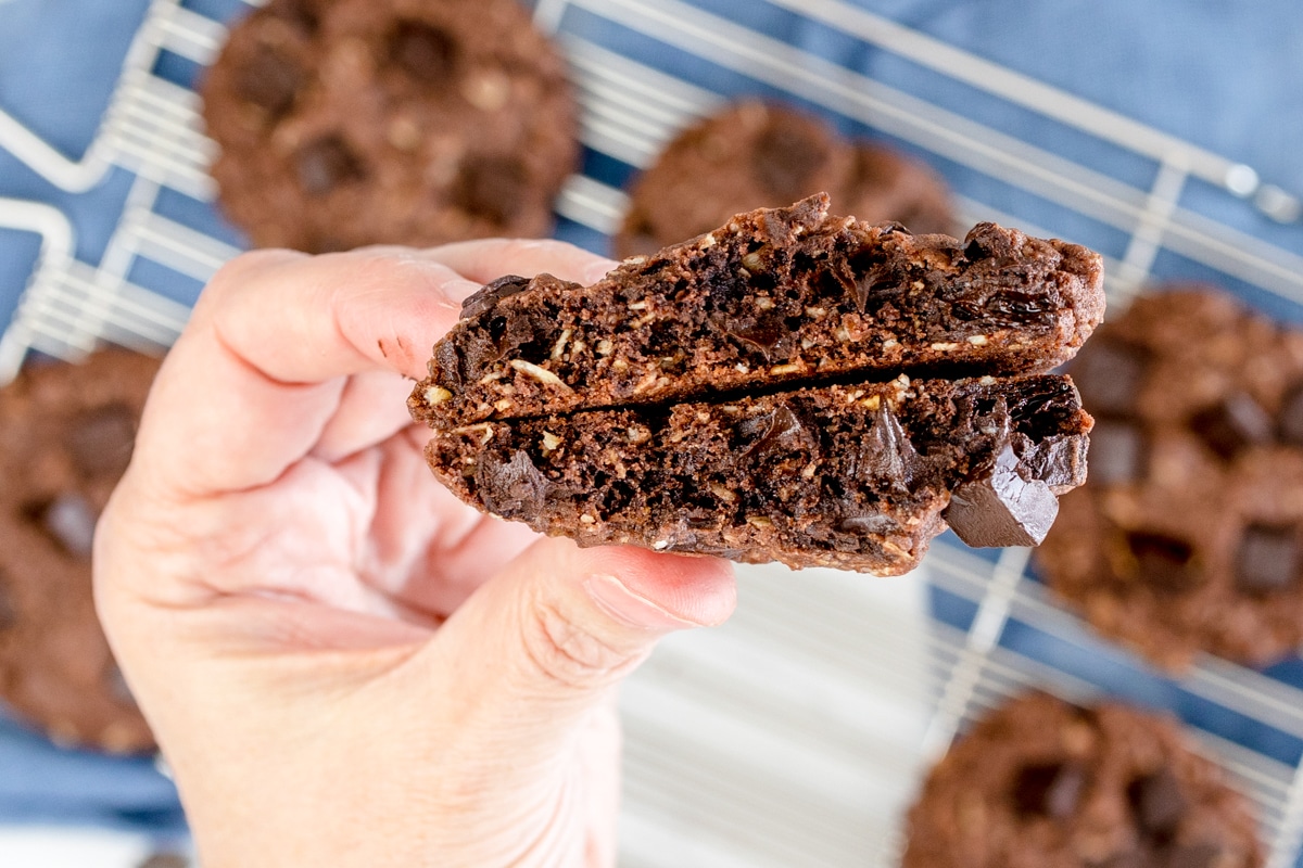 Close-up of a chocolate oatmeal cookie broken in half and being held in mid-air. 