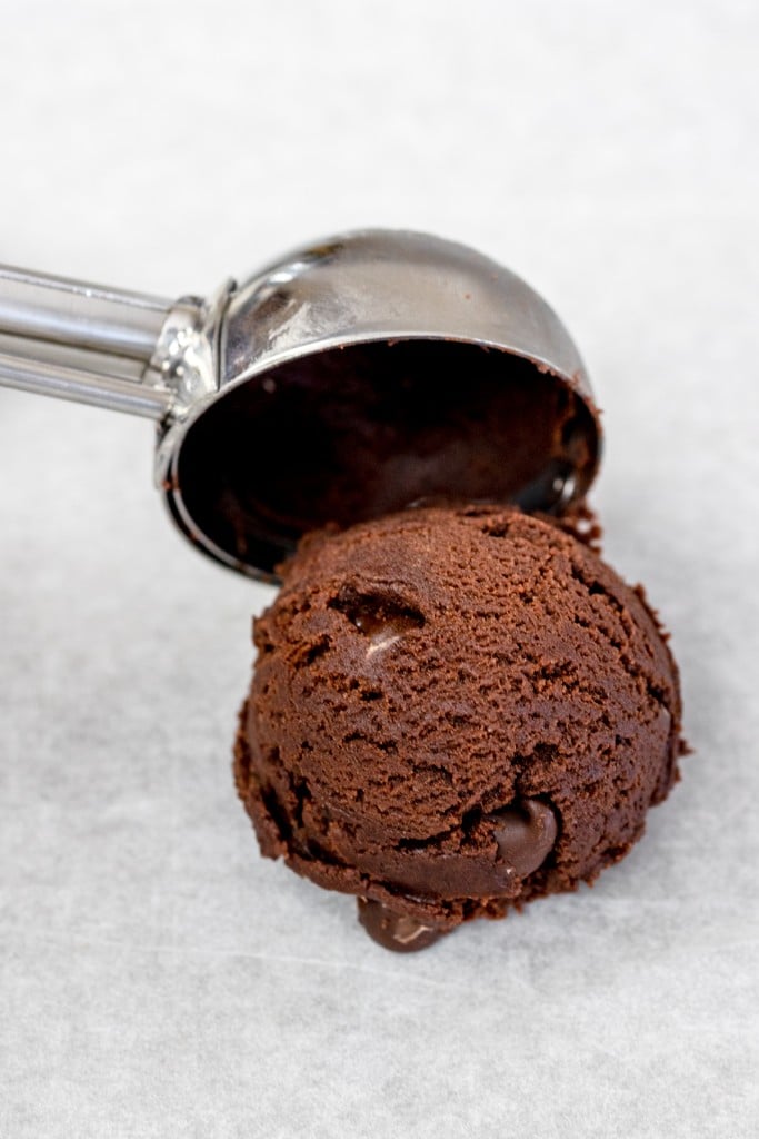 Close up of a cookie scoop putting a scoop of chocolate chunk cookie dough onto a baking sheet lined with parchment paper. 