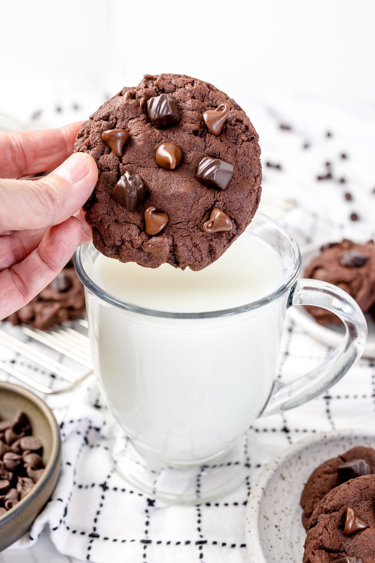 Close up of a chocolate pudding cookie being held above a glass of milk. 