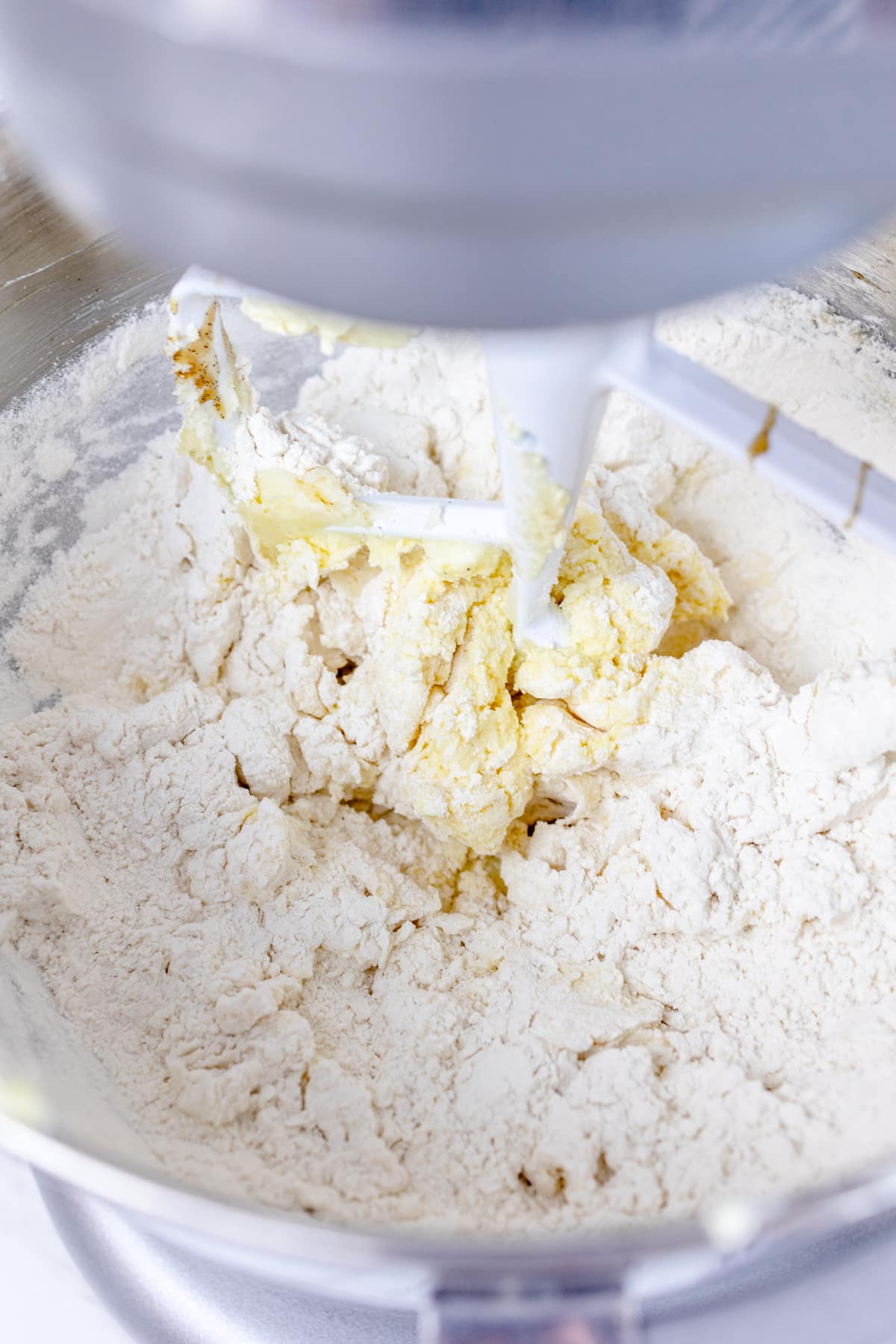 Close up of flour mixture in a stand mixer mixing bowl with a paddle attachment mixing the mixture. 