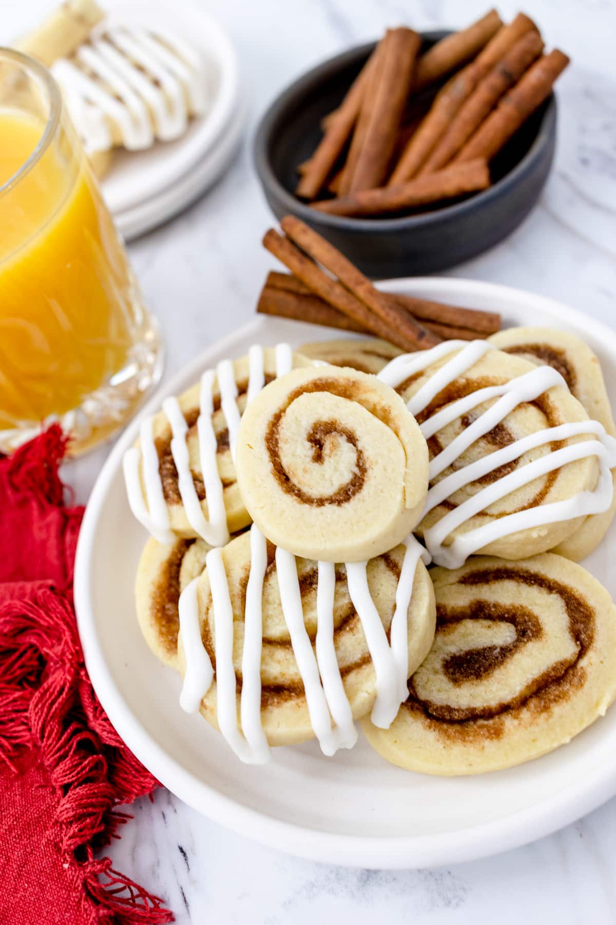 A plate filled with cinnamon swirl cookies with a bowl of cinnamon sticks next to it.