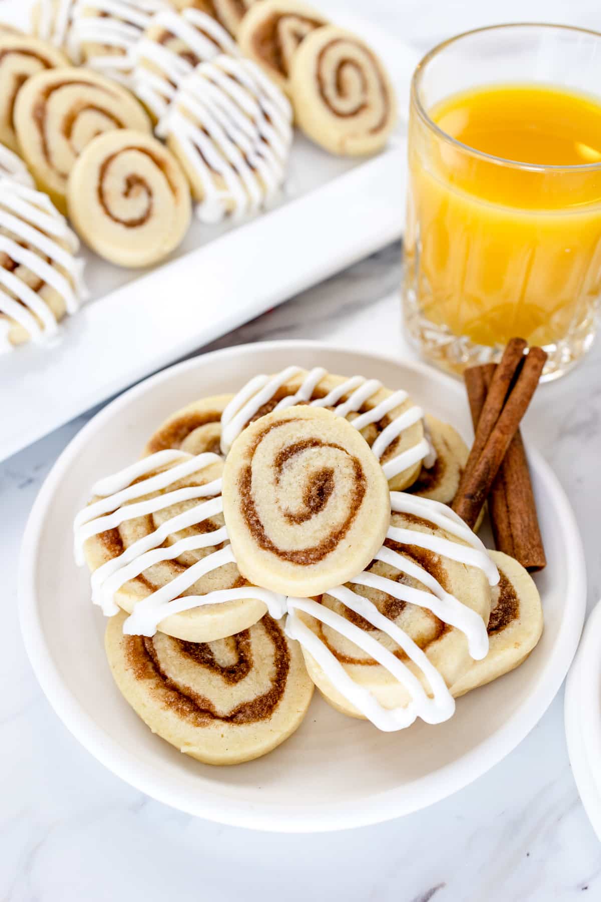 A plate filled with cinnamon roll cookies next to a glass of orange juice. 