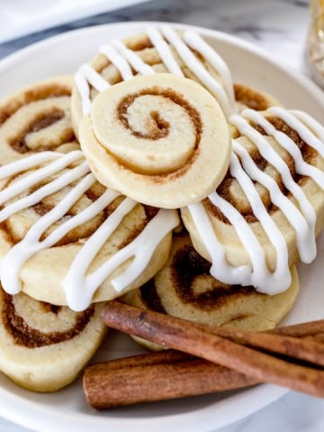 Close up of Cinnamon Roll Cookies on a plate with cinnamon sticks on the plate too.