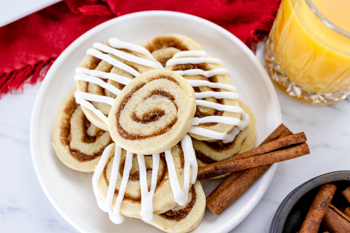 Top view of Cinnamon roll cookies on a plate with cinnamon sticks next to them. 