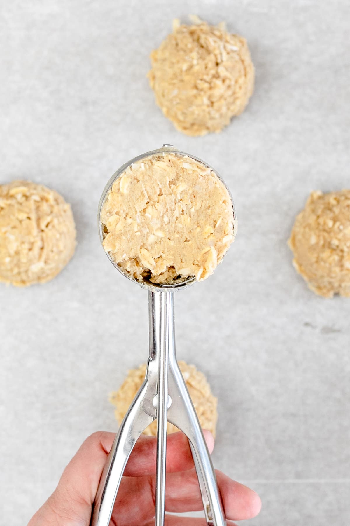 Top view of a cookie scoop being held in mid-air, full of oaty cookie dough. 