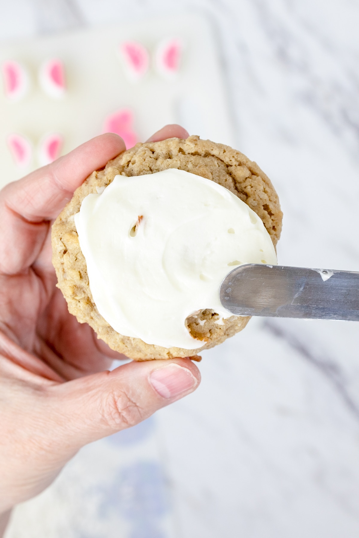 Top view of an oatmeal cookie having a white frosting spread on it with a knife. 