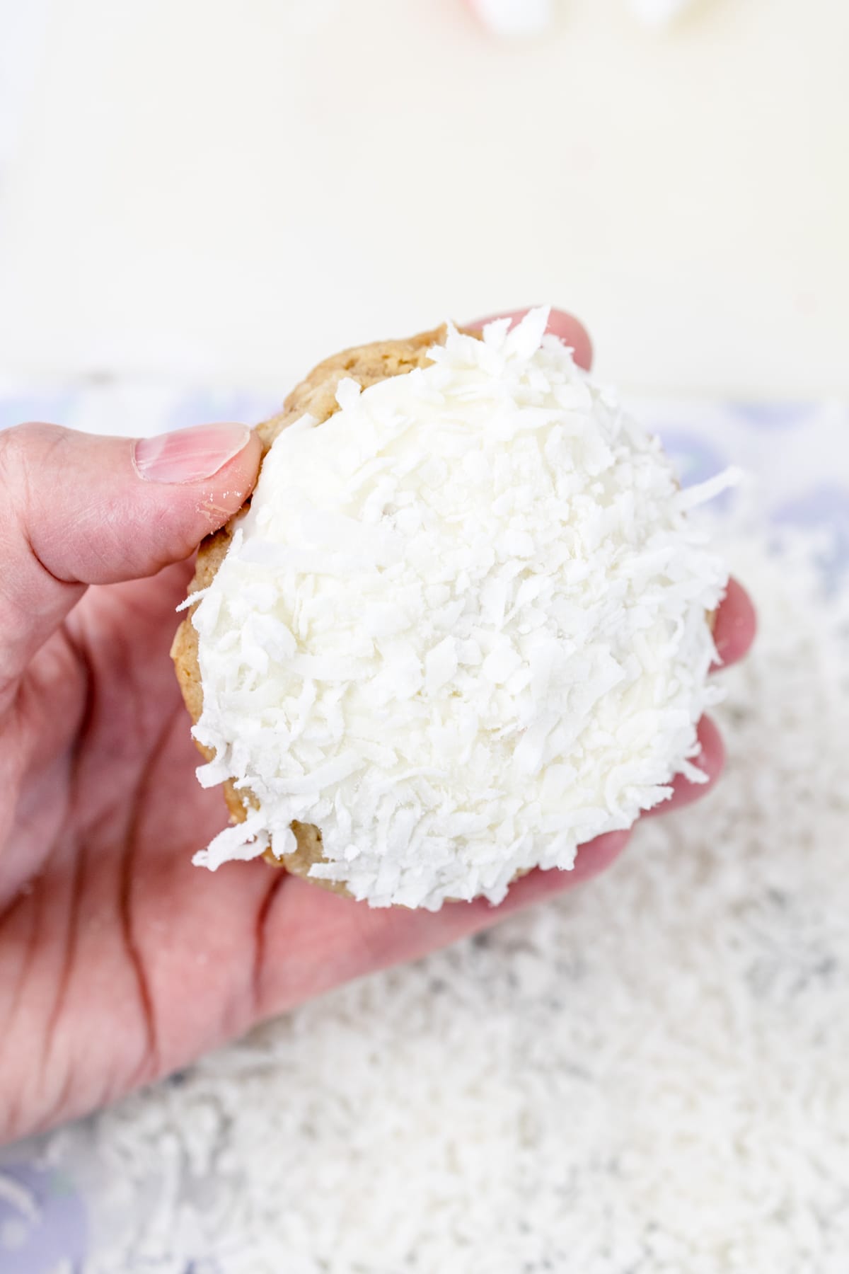 Top view of a hand holding an oatmeal cookie covered in shredded coconut.