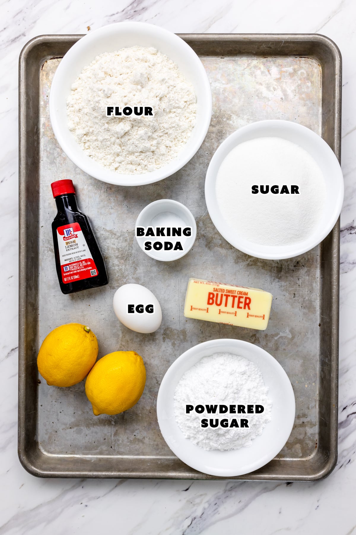 Top view of ingredients needed to make Lemon Crinkle Cookies in glass bowls on a baking tray. 