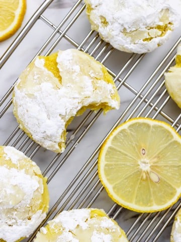 Top view of Lemon Crinkle Cookies ona. wire rack next to a slice of lemon.