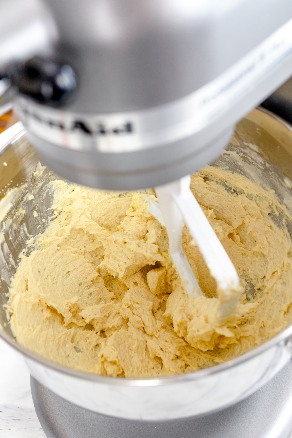 Close up of stand mixer with lemon cookie dough being mixed in the bowl. 