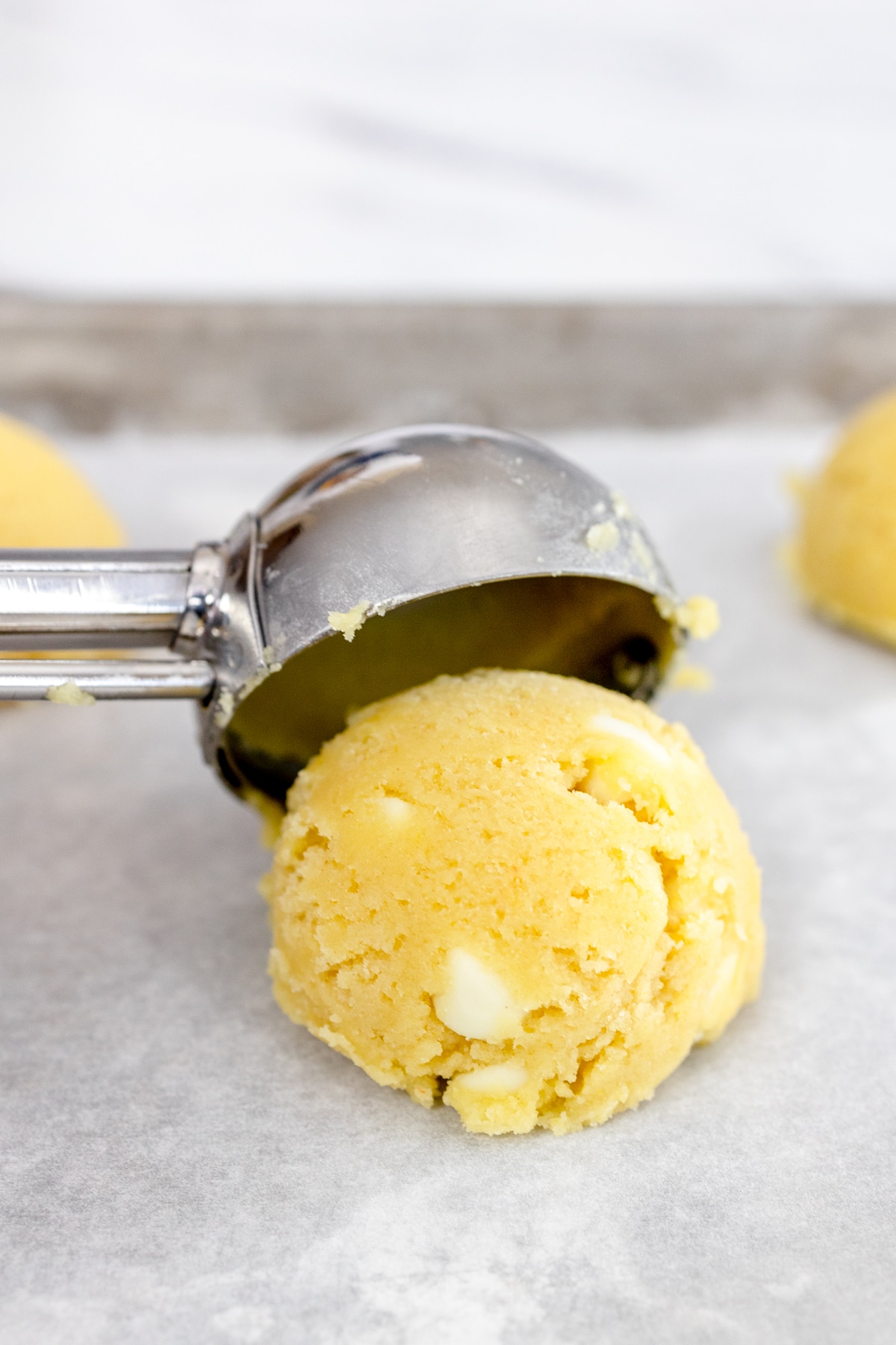 Close up of lemon cookie dough ball being scooped onto a baking tray lined with parchment paper. 