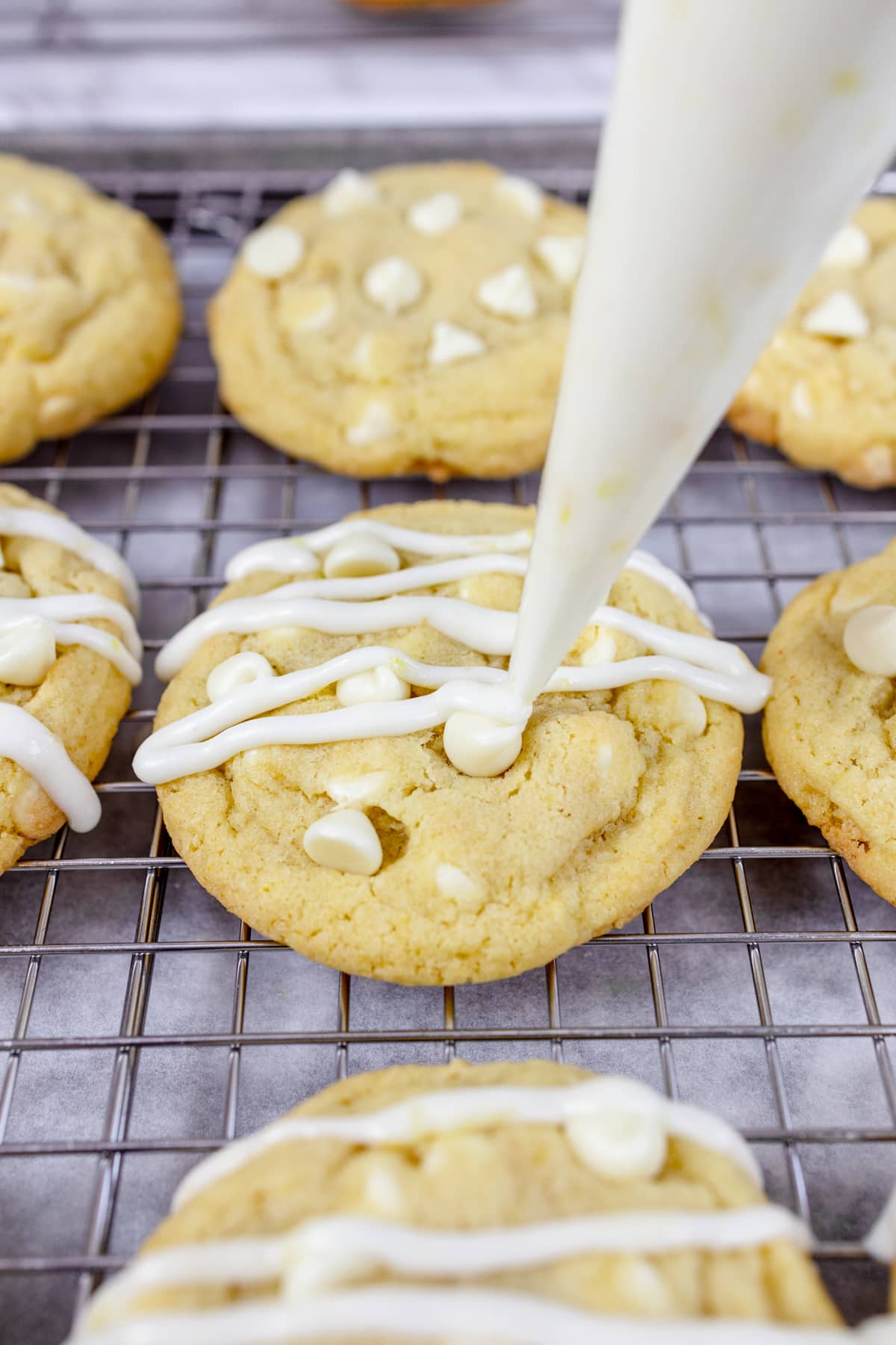 Close up of lemon white chocolate cookies being topped with an icing drizzle applied with a piping bag.