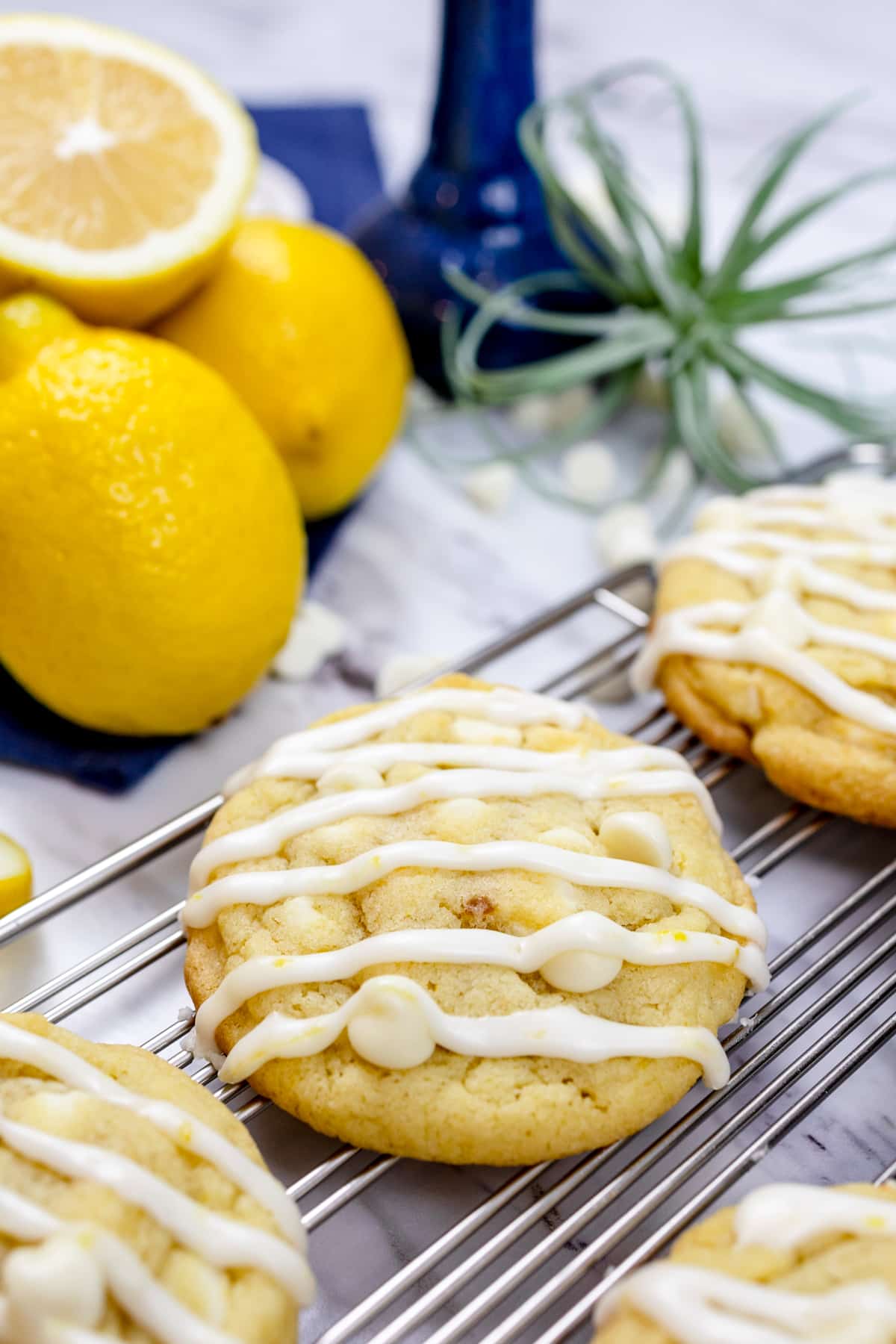 Lemon white chooclate chip cookies on a wire rack next to some lemons. 