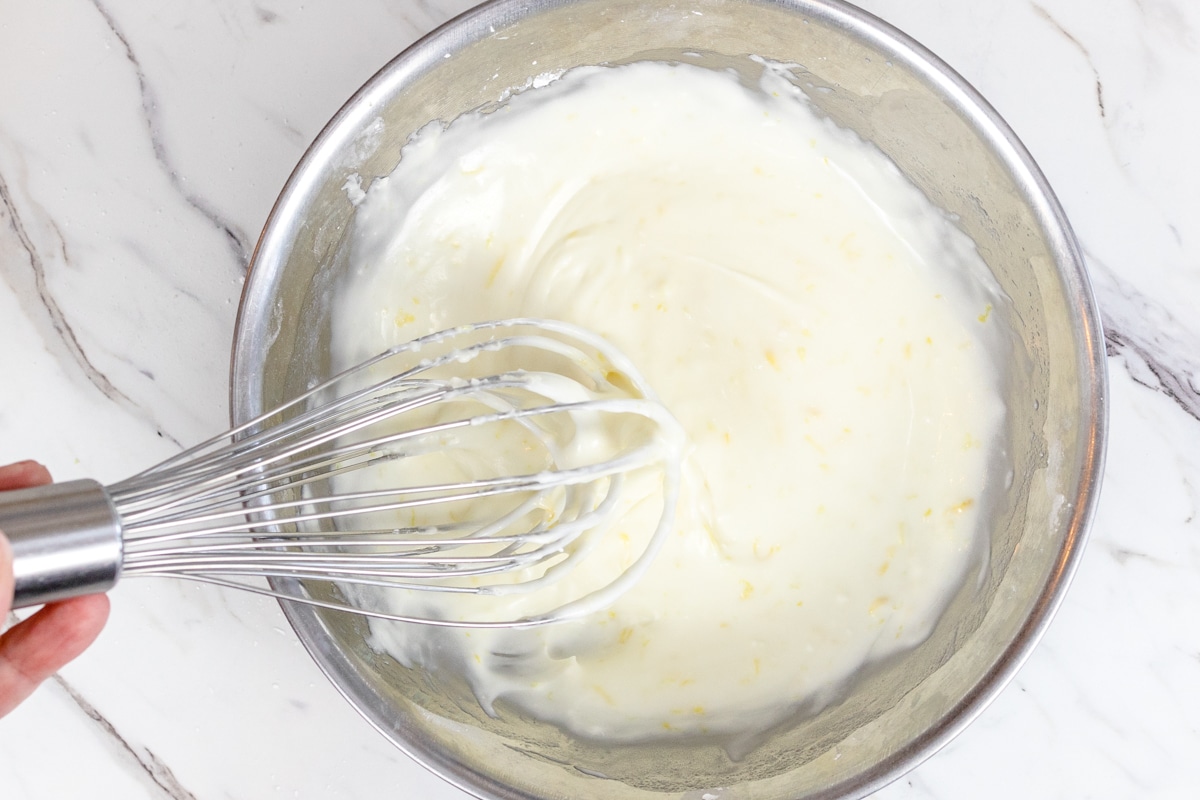Top view of glass mixing bowl with icing being mixed with a whisk. 