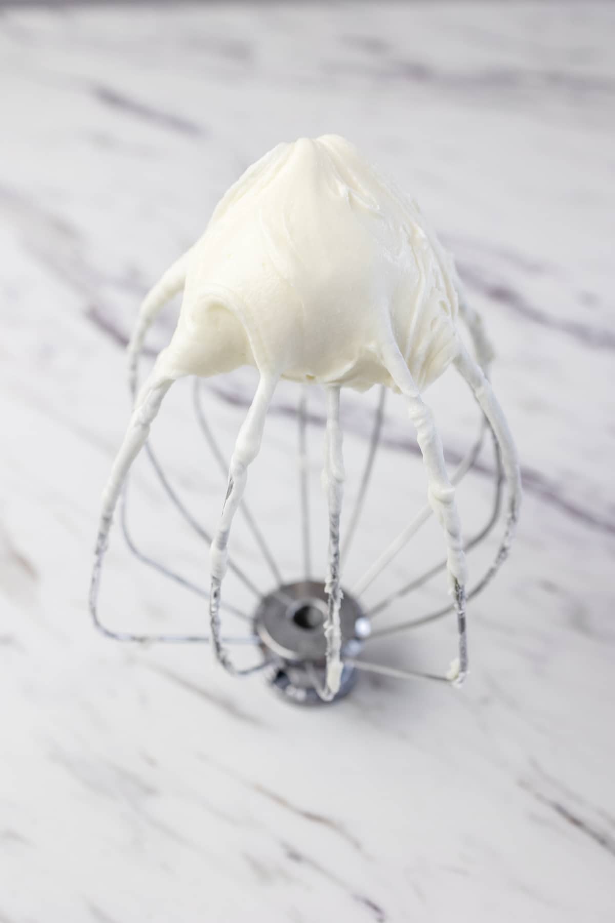 Close up of standing mixer whisk attachment with white frosting on it. 