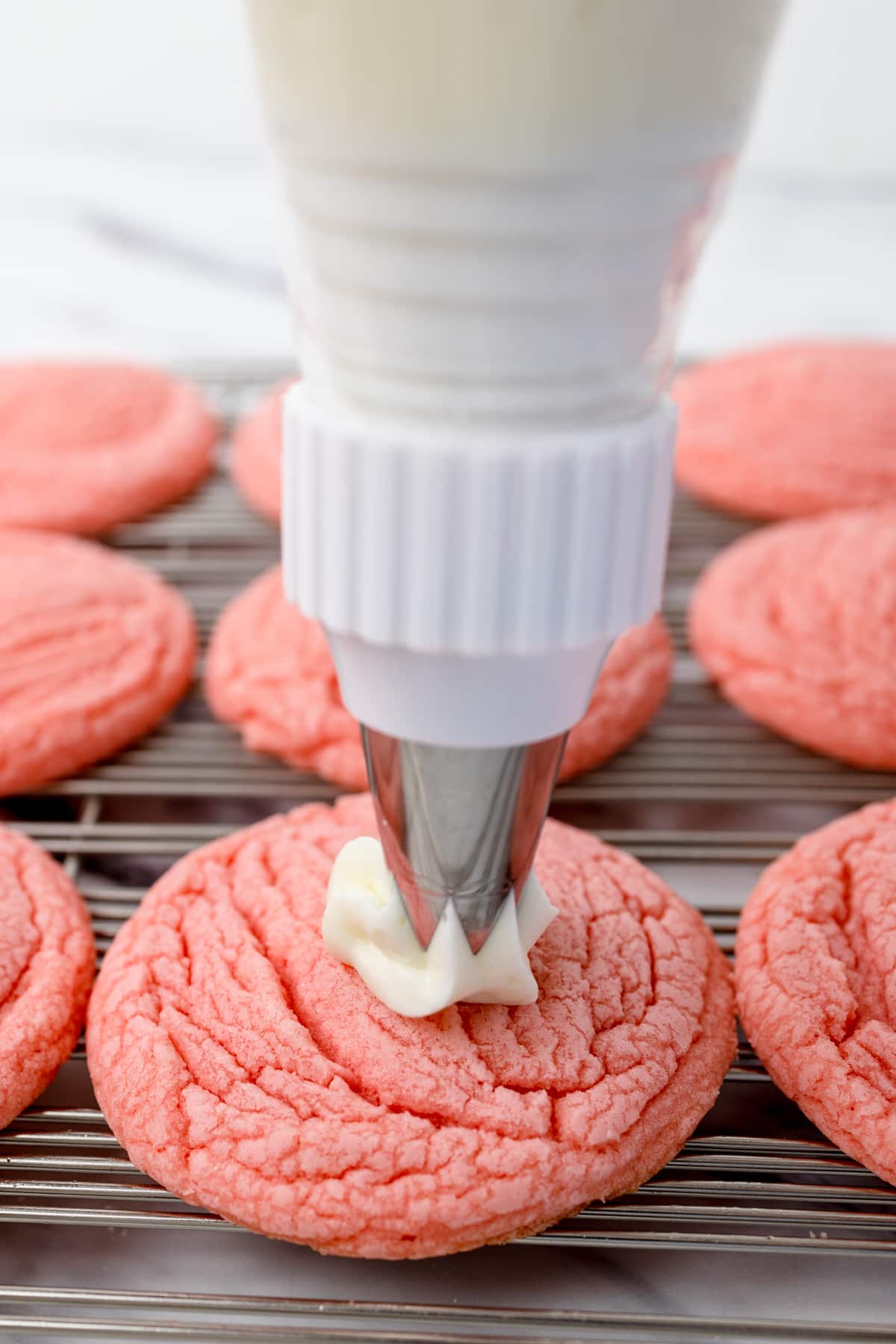 Close up of pink cookie being frosted with frosting with a piping bag. 