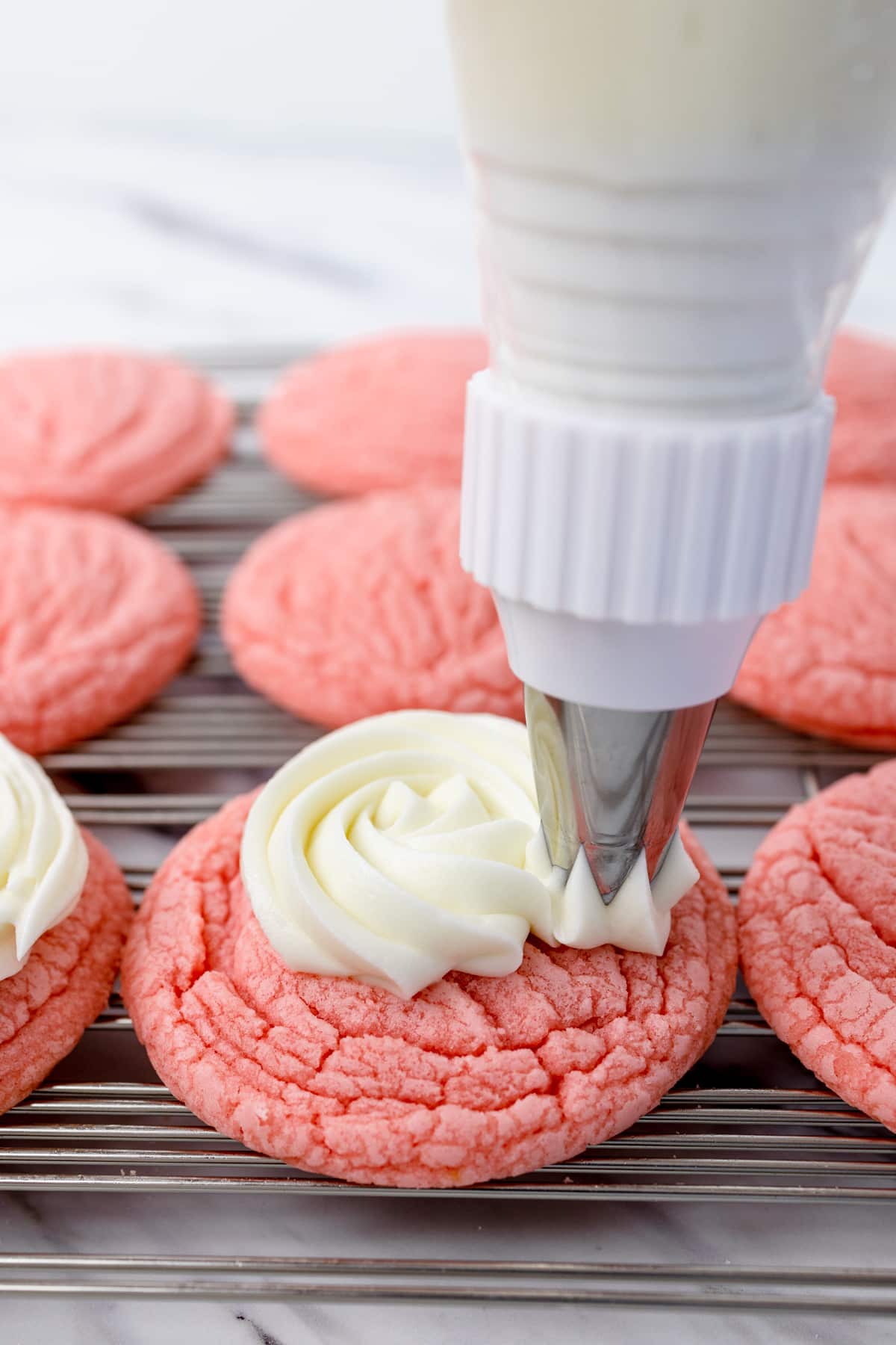 Close up of pink cookie being frosted with frosting with a piping bag and a large star tip.