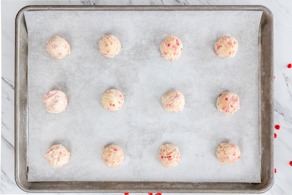Top view of a baking tray filled with red hot cookie dough balls. 
