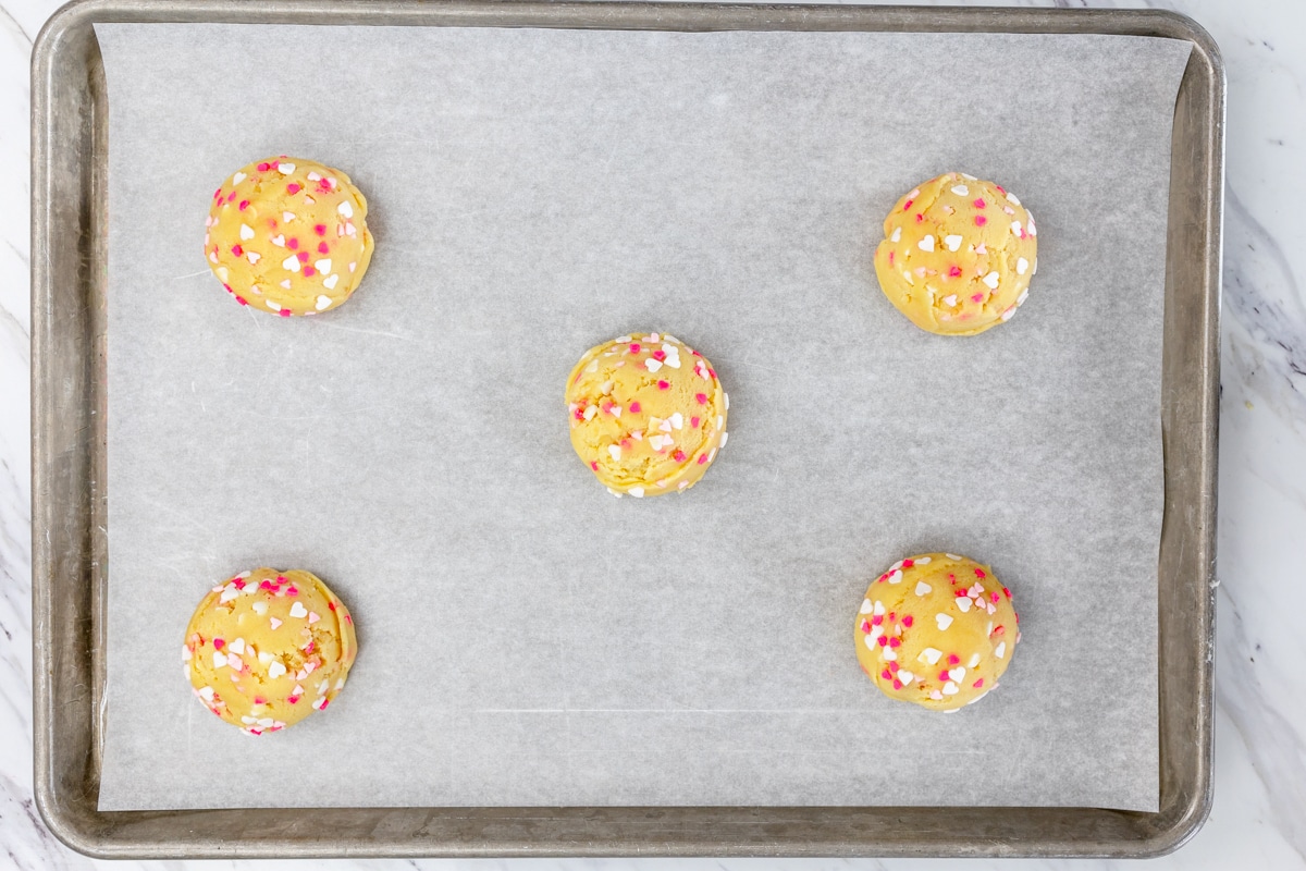 Top view of sprinkle sugar cookie dough balls on a baking tray lined with parchment paper. 