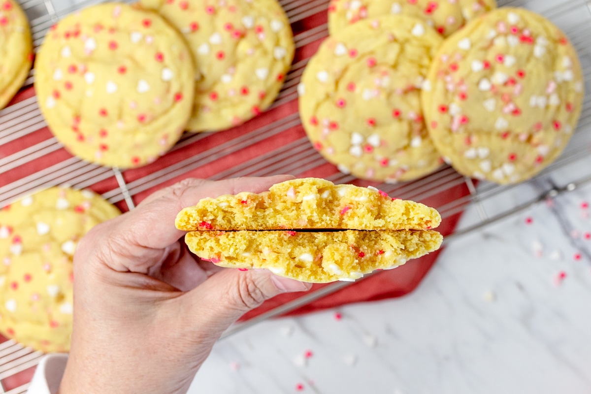Close-up of someone holding two halves of a Sprinkle Sugar cookie so you can see the soft inside. 