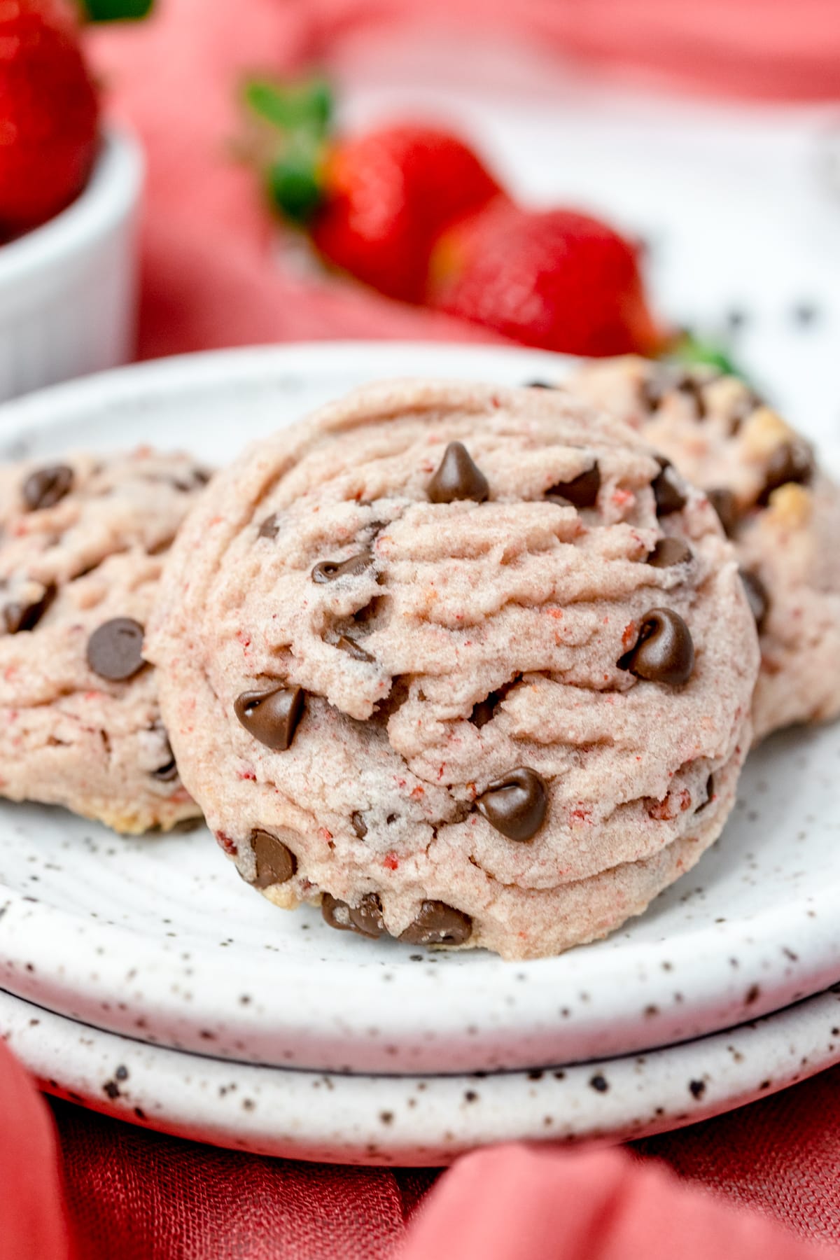Close up of strawberry chocolate chip cookies in a pile on a plate. 
