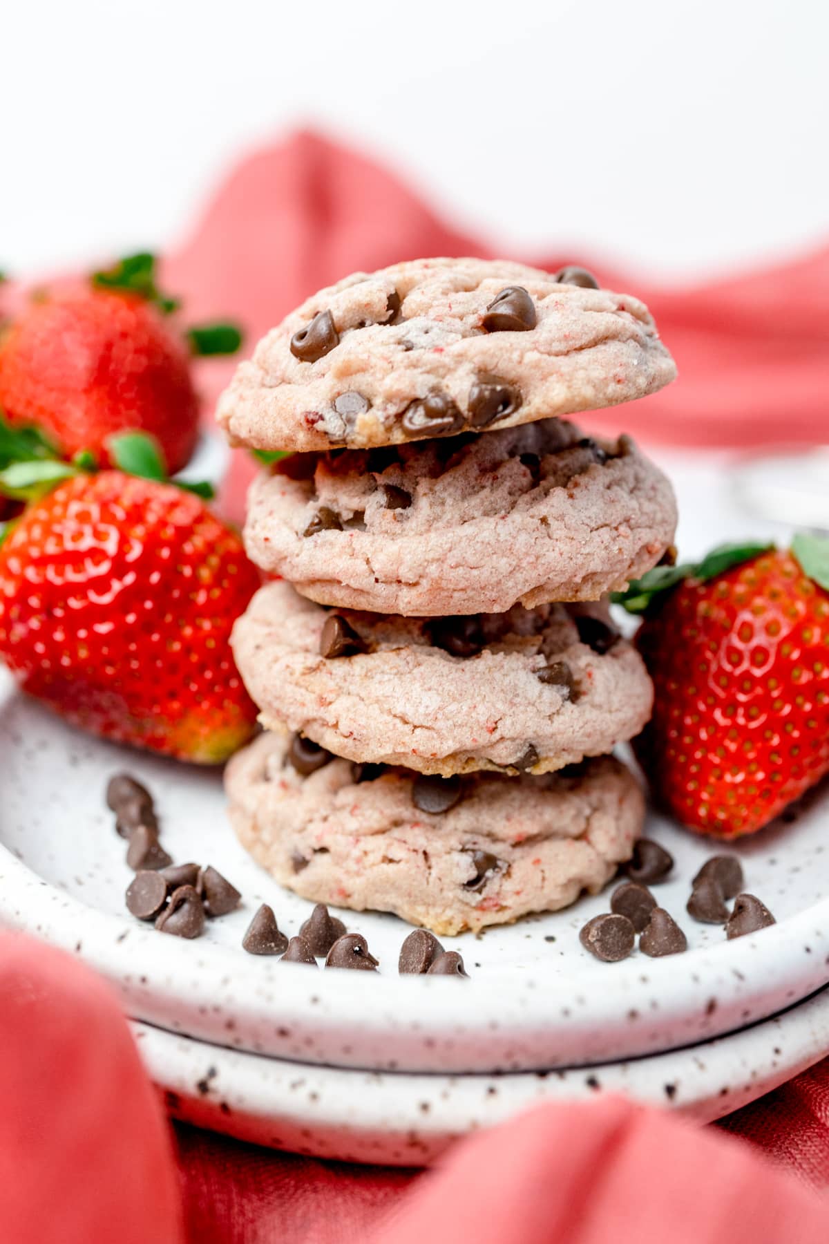Stack of strawberry chocolate chip cookies on a white plate surrounded by strawberries.  