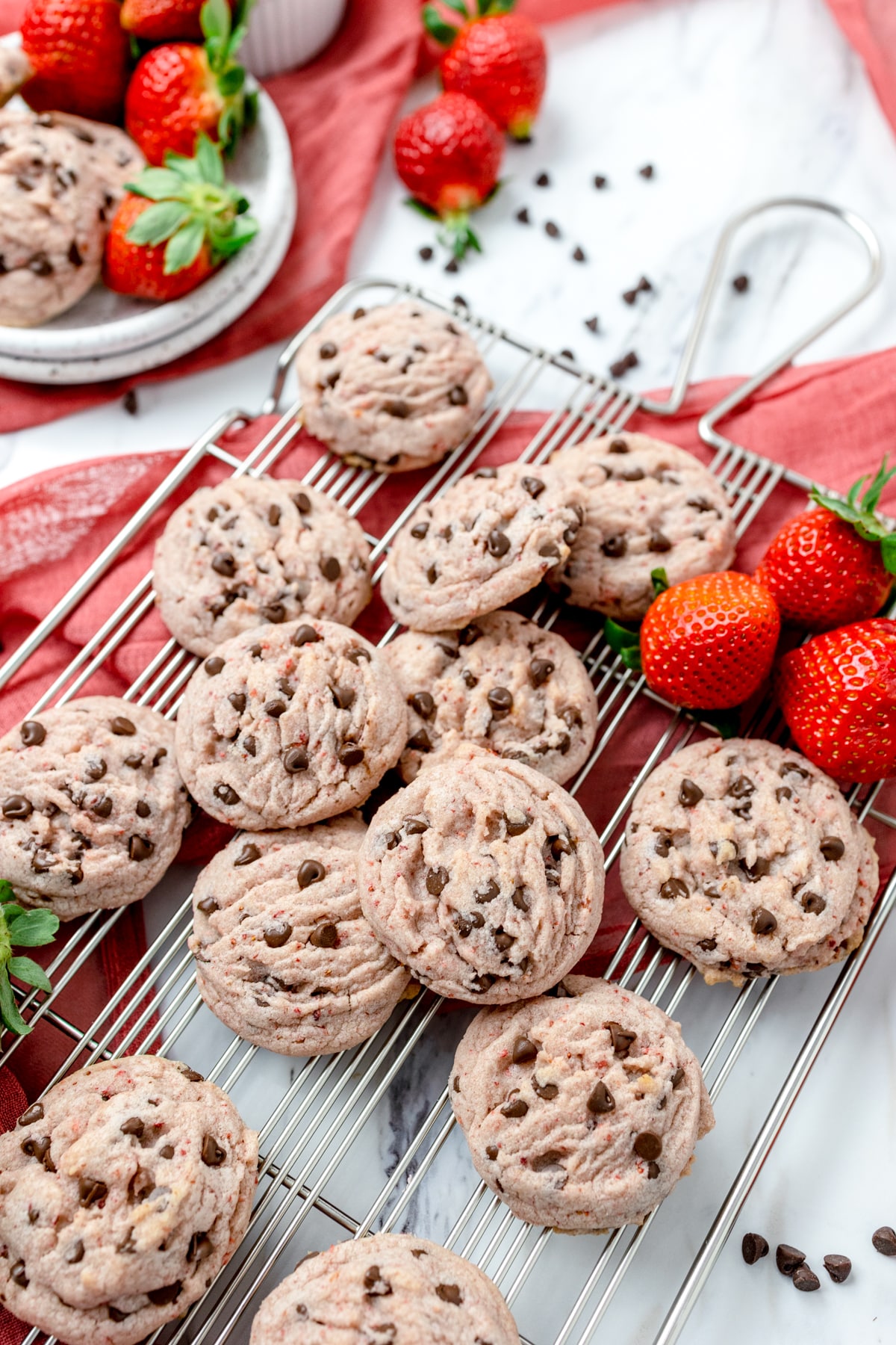 Top view of strawberry chocolate chip cookies scattered on a table with strawberries next to them.