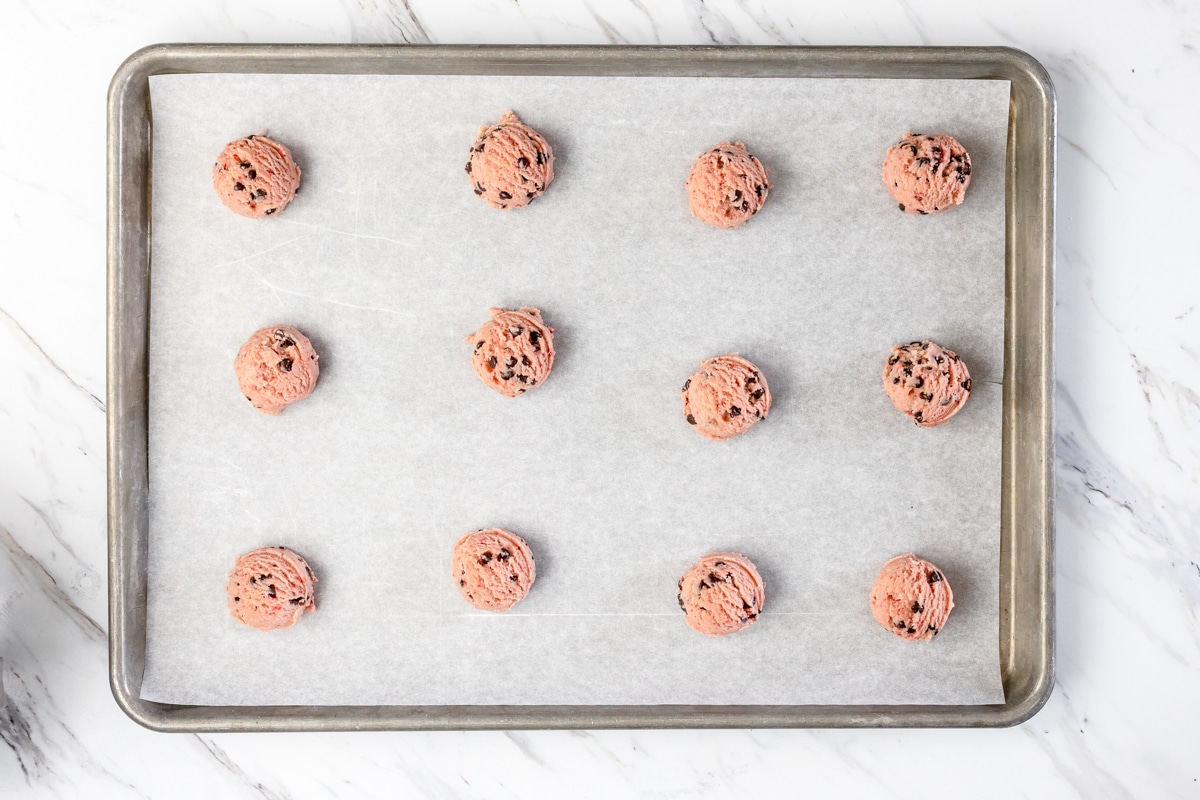 Top view of a baking tray covered with balls of strawberry chocolate chip cookie dough. 