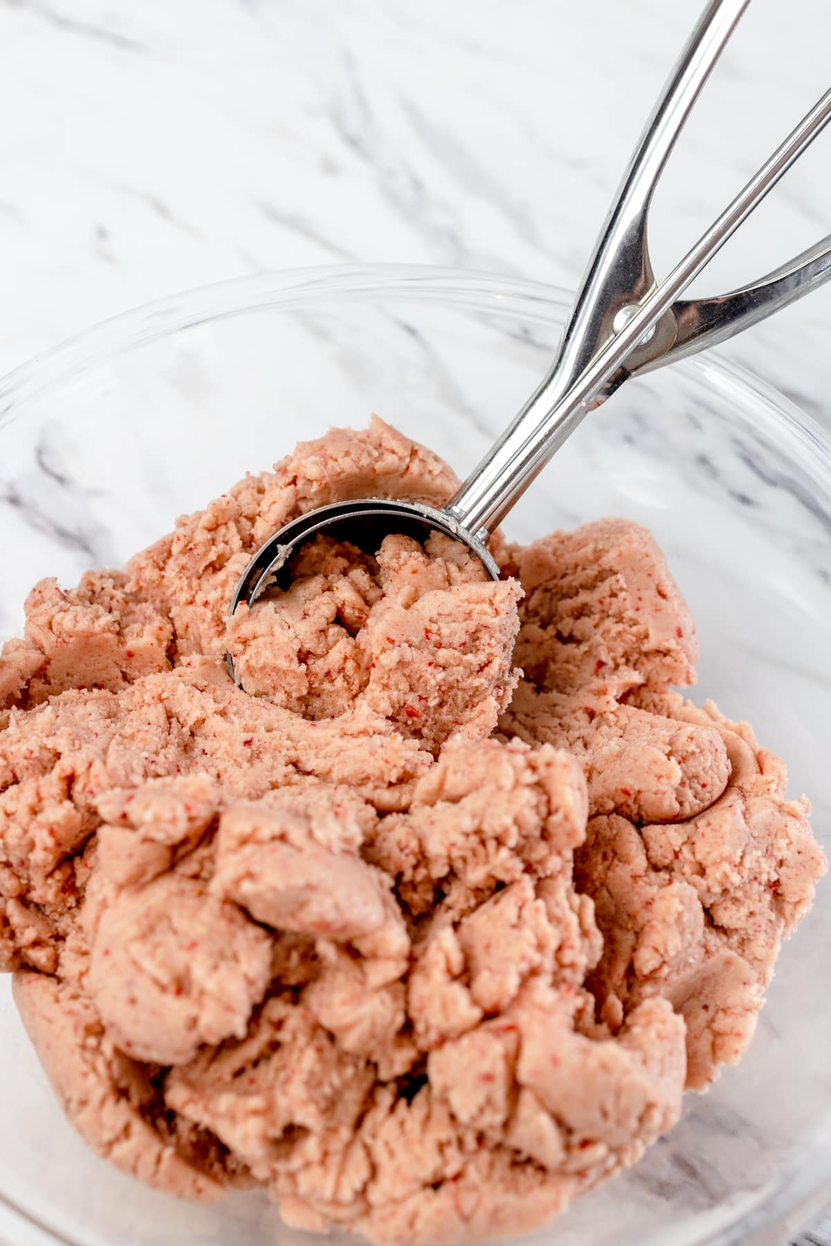Close up of a cookie scoop scooping out strawberry sugar cookie dough.