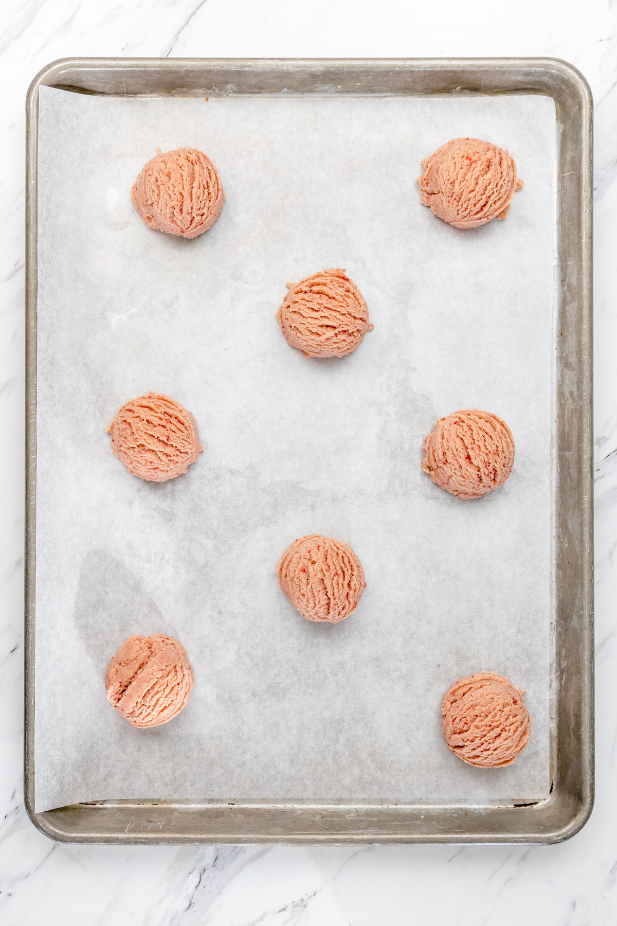 Top view of a baking tray lined with strawberry sugar cookie dough balls. 