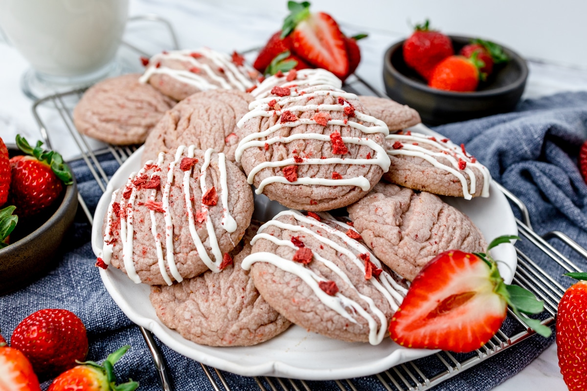 White plate filled with a pile of strawberry cookies with drizzle and strawberry pieces on them. 