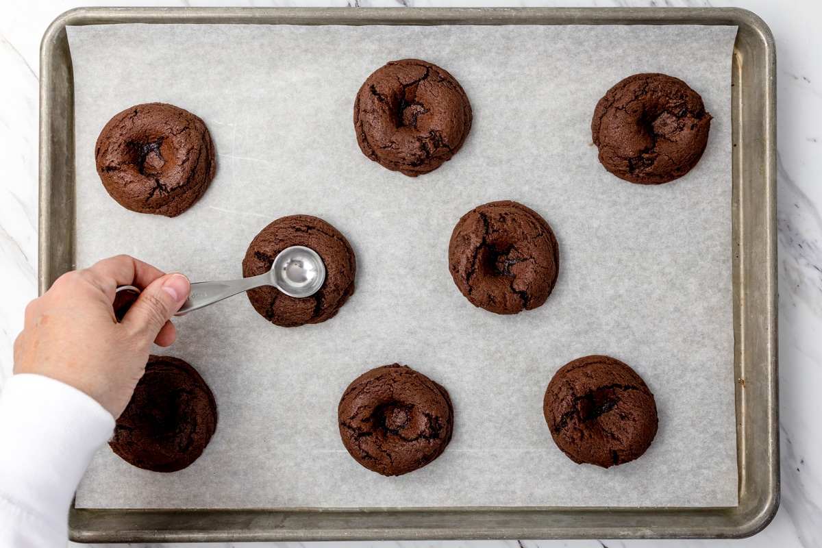 Top view of freshly baked chocolate cookies on a tray being flattened with a small spoon. 