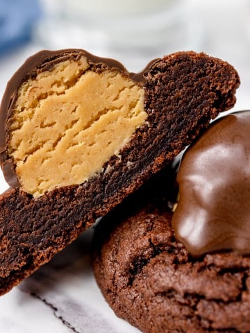 Close up of Buckeye Cookies, one that's been cut in half so you can see the peanut butter underneath the ganache.