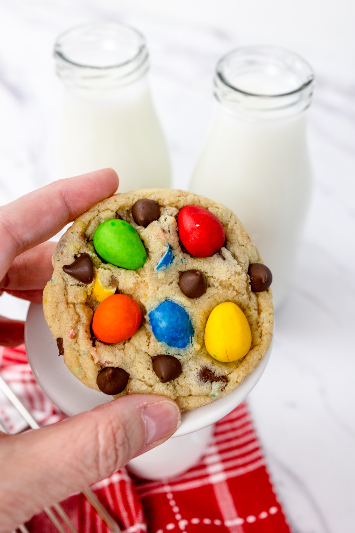 Close up of a Mini Egg Cookie being held in mid-air in front of two bottles of milk.