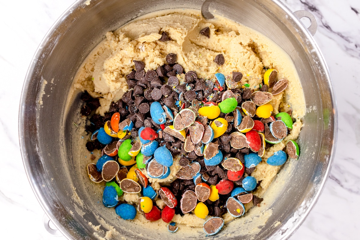 Top view of mixing bowl with cookie dough topped with chocolate chips and crushed Cadbury Mini Eggs in it. 