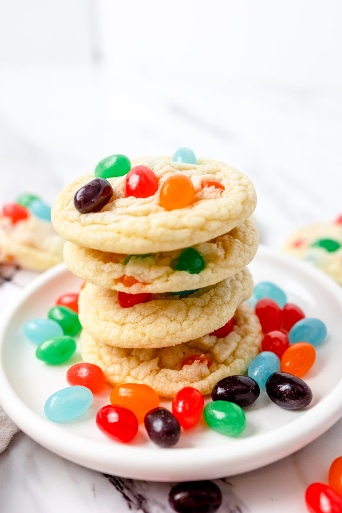 close up of a stack of cookies with Jelly Beans in them on a white plate with Jelly Beans around them. 