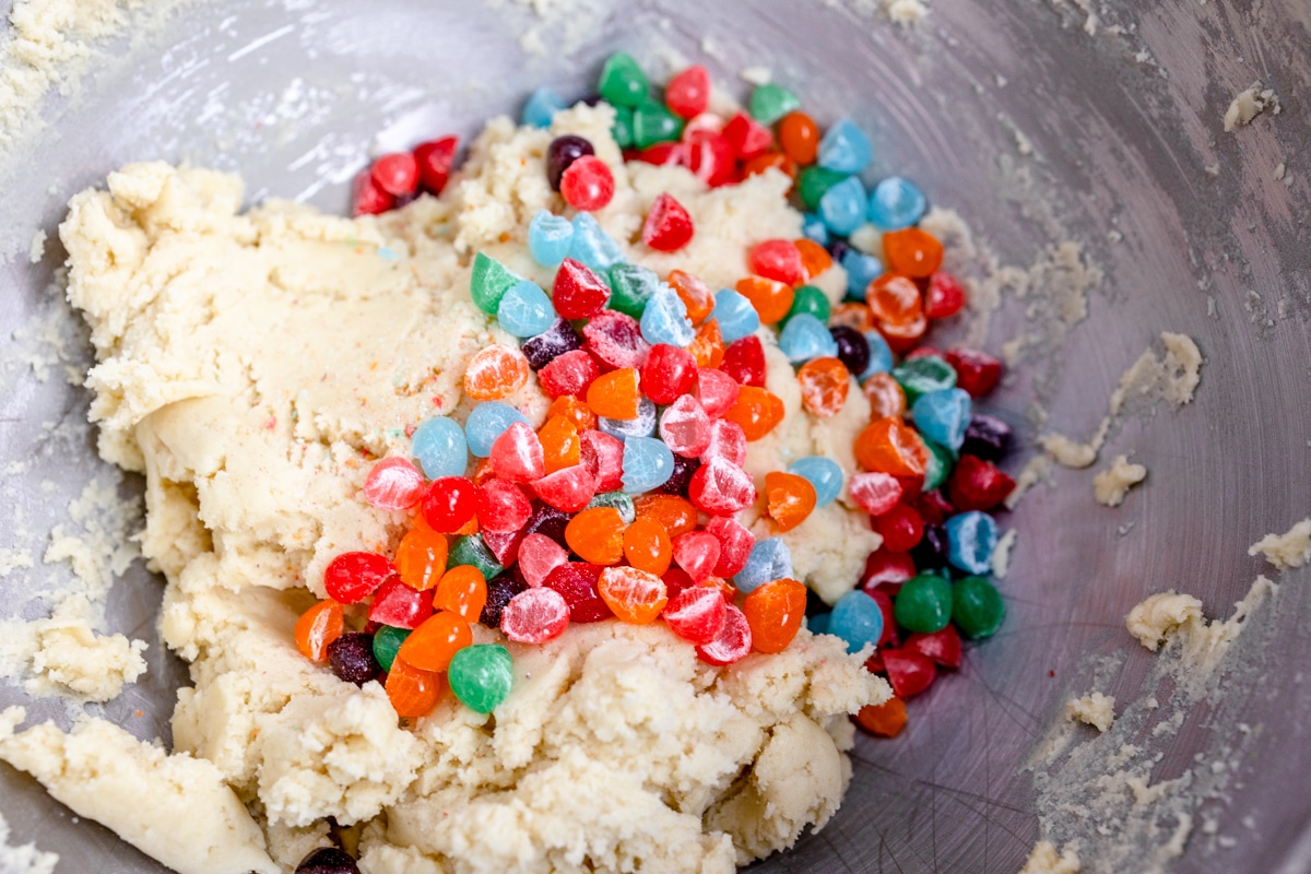 Top view of mixing bowl with cookie dough in it and halved Jelly Beans on top. 