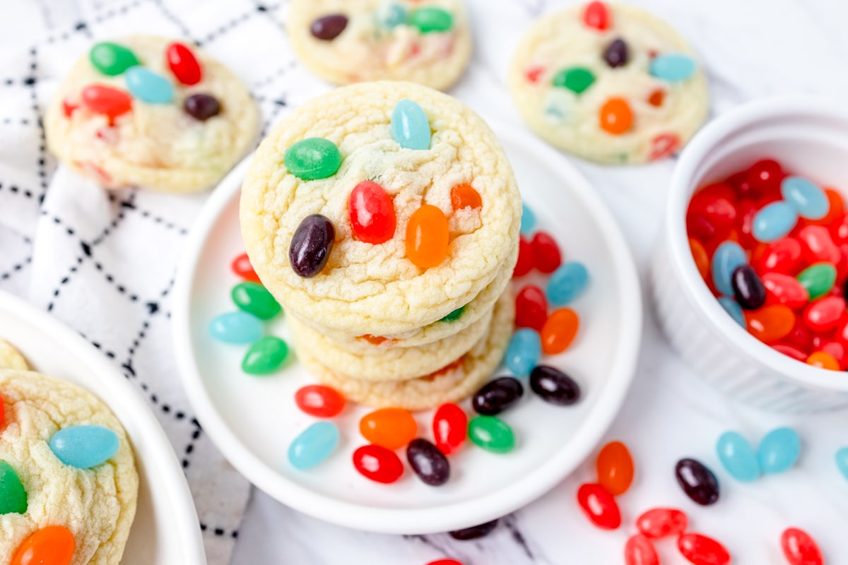 Top view of a stack of cookies with Jelly Beans in them and Jelly Beans on the work top and on the plate. 
