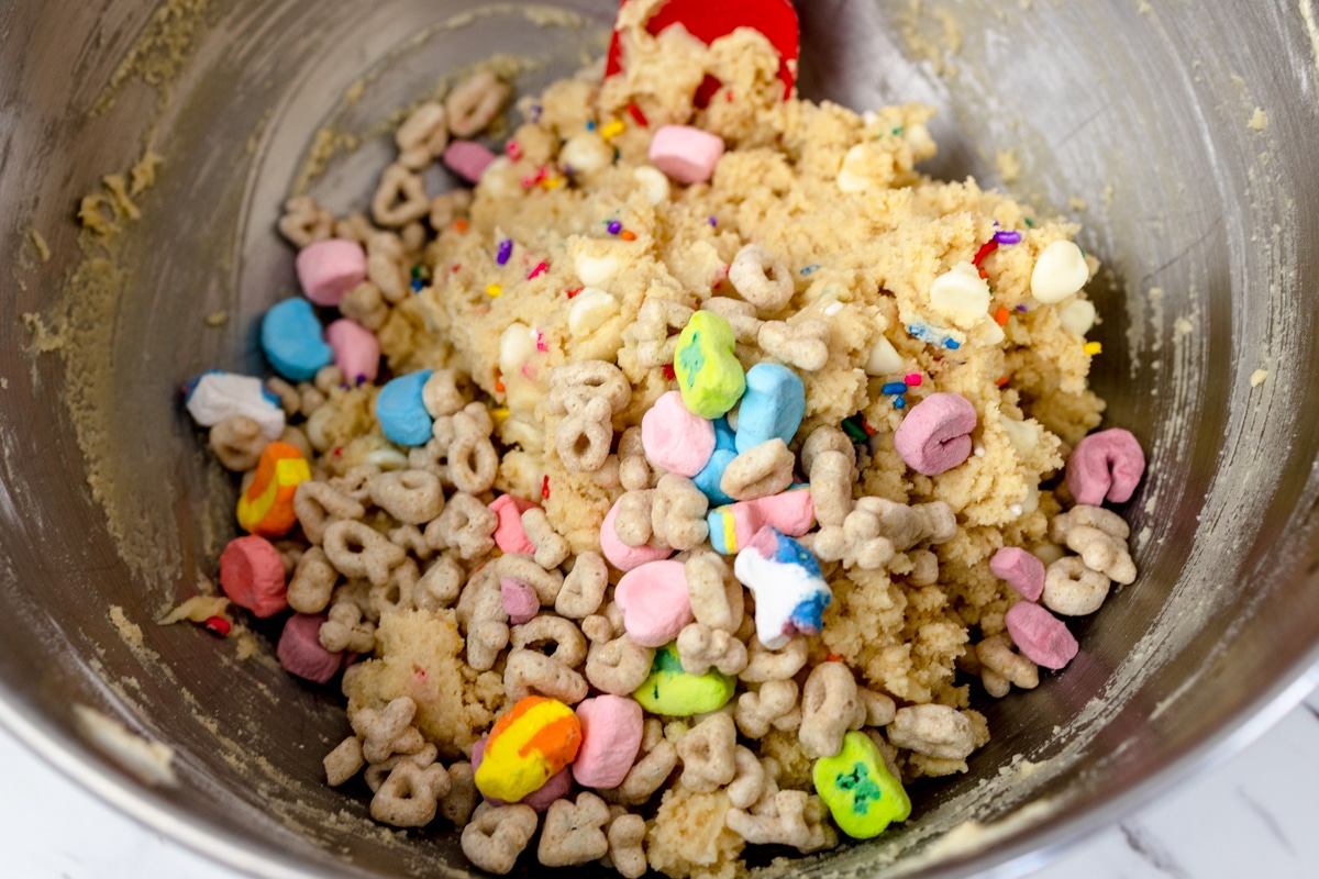 Top view of mixing bowl with cookie dough, white chocolate chips, and sprinkles in it with lucky charms marshmallows on top.