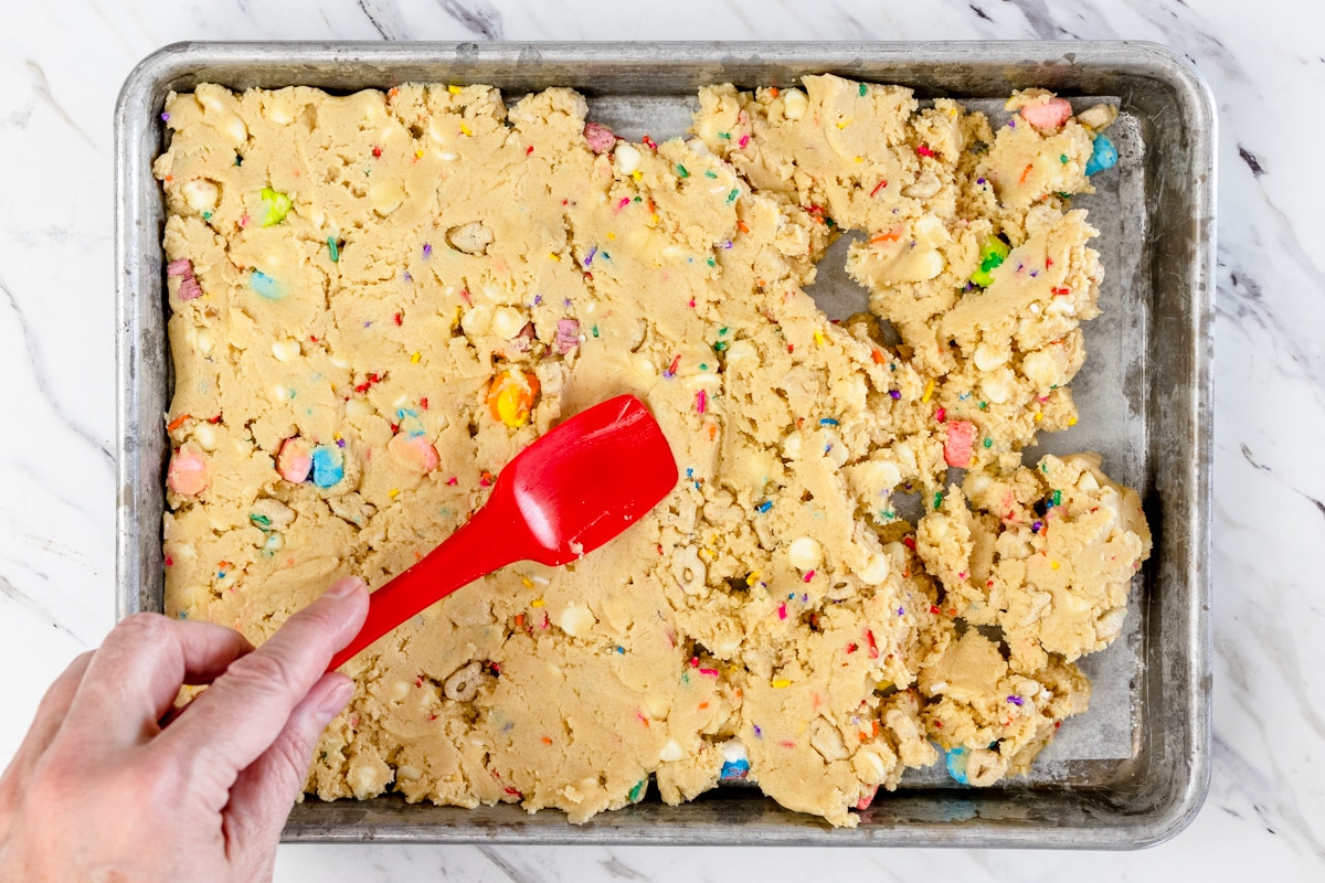 Top view of lucky charms cookie dough being spread into a baking pan. 